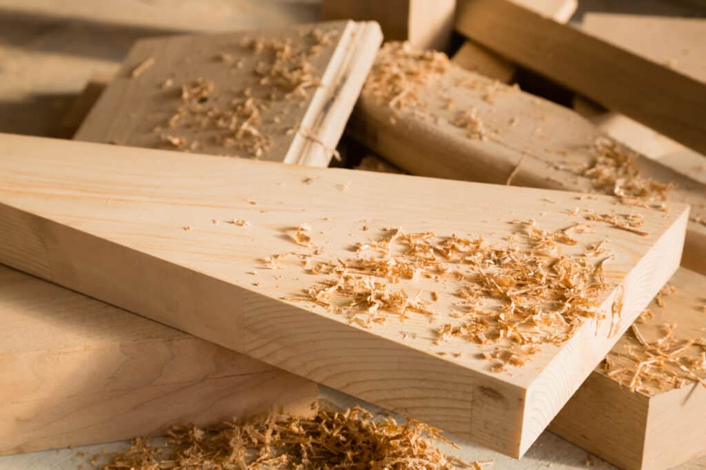 Copeaux de bois : L'atelier de menuiserie à l'œuvre Copeaux de bois clair éparpillés sur des planches en bois brut empilées. Scène d'atelier de menuiserie avec lumière et ombres.