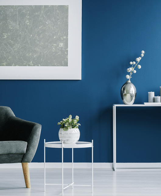 Décoration salon moderne bleu: idées design intérieur Salon moderne: murs bleu marine. Fauteuil gris, table blanche avec plante. Tableau abstrait argenté encadré. Console blanche avec vase et bougies.