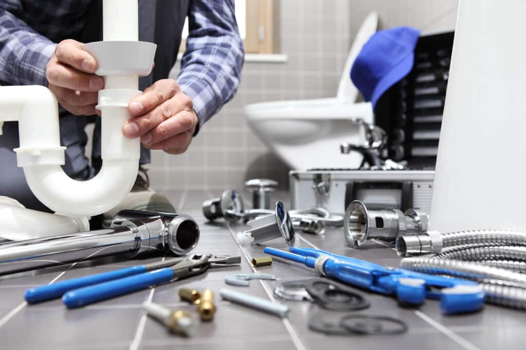 Réparation Plomberie : Assemblage Tuyaux PVC dans une salle de bain Plombier en chemise à carreaux assemblant des tuyaux PVC blancs. Outils de plomberie et toilettes visibles sur un sol carrelé.